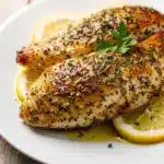 Baked Greek chicken breast with a golden herb crust and fresh oregano.