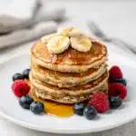 Banana oat pancakes with maple syrup and blueberries on a white plate