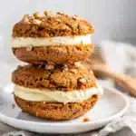 Moist carrot cake whoopie pies with creamy frosting filling on rustic board.