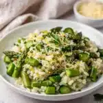 Creamy asparagus risotto with Parmesan in a white bowl on a wooden counter