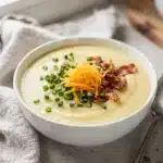 Creamy potato soup garnished with crispy bacon and cheddar cheese in a rustic bowl.