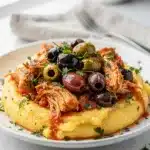 Crockpot tomato olive chicken with savory sauce over creamy polenta or pasta.