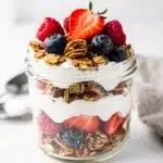 Greek yogurt parfait with granola and fresh berries in a glass jar.