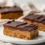No bake peanut butter bars with chocolate topping on a white plate.
