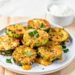 Crispy parmesan zucchini bites with melted cheese on a rustic wooden board.