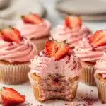 Strawberry cream cupcakes with pink frosting and fresh fruit garnish.