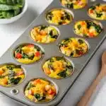 Golden brown veggie egg muffins with spinach and cheddar cheese in tin.