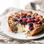Baked oatmeal with berries in a rustic dish features honey yogurt and almonds.