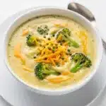 Creamy broccoli cheddar soup recipe in a rustic white bowl with bread.