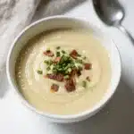 Creamy potato leek soup in a white bowl with chives and cream