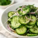 Crisp cucumber salad with red onion and fresh dill in a white bowl.