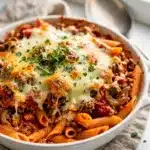 Easy pasta bake with golden cheese, red sauce, and penne on white plate.