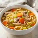 Easy Cozy Chicken Noodle Soup recipe with tender chicken and carrots in golden broth.