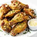 Crispy garlic parmesan chicken wings with parsley on a rustic wooden board.