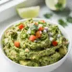 Creamy homemade guacamole with fresh lime in a rustic stoneware bowl.