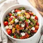 Colorful Italian pasta salad with rotini, salami, and fresh vegetables in a bowl.