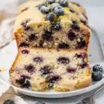 Moist lemon blueberry loaf cake with glaze on rustic wooden cutting board