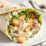 Make ahead chicken Caesar wrap sliced open on a rustic wooden board.