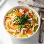 Make ahead cozy chicken noodle soup in a rustic white bowl with vegetables