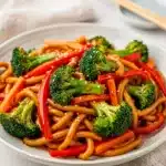 Meal prep udon stir fry with chicken and vegetables in separate compartments.