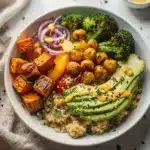 Colorful roasted veggie grain bowl with quinoa, avocado, and lemon tahini sauce.