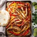 Sheet pan chicken fajitas with peppers onions and toppings on a wooden table