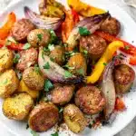 Crispy sausage and tender roasted vegetables on a white sheet pan