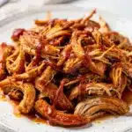 Close up of tender shredded BBQ chicken in a rustic white ceramic bowl
