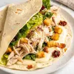 Sliced chicken caesar wrap on a rustic board with creamy dressing.