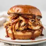 Slow cooker BBQ chicken sandwich with glossy sauce on toasted brioche bun