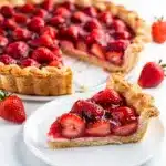 Golden flaky strawberry pie with glossy red filling and whipped cream garnish.