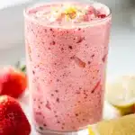 Refreshing strawberry lemonade smoothie in a tall glass with fruit garnish.
