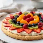 Sweet fruit pizza sugar cookie topped with fresh colorful berries and creamy frosting.