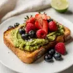 Avocado toast topped with fresh berries and seeds on rustic bread