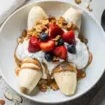 Healthy breakfast banana split bowl with yogurt, fresh berries, and crunchy granola.