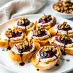 Rustic fig goat cheese crostini appetizer with jam and walnuts on slate.