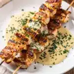 Grilled chicken skewers with garlic parmesan sauce on a rustic wooden board.