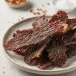Homemade beef jerky recipe on a rustic wooden board with spices.