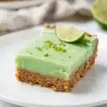 Creamy key lime pie bars with whipped cream on a rustic wood background.