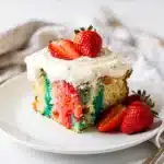 Colorful strawberry jello poke cake slice with fluffy frosting and fresh berries