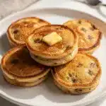Mini banana pancake bites with maple syrup on a white plate.