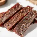 Old fashioned peppered beef jerky recipe with glossy leathery textures on rustic board
