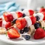 Patriotic fruit skewers with strawberries bananas blueberries and marshmallows on a white platter