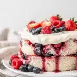 Summer berry poke cake with juicy holes and fluffy whipped cream topping