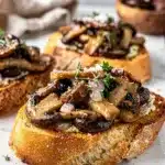 Savory wild mushroom bruschetta with thyme and Parmesan on toasted baguette slices.