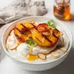 Grilled peaches yogurt with honey, almonds, and mint garnish.